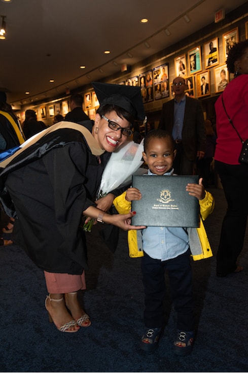 A woman in graduation cap and gown and her little son holding up the diploma